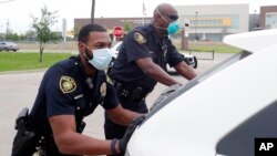 En esta imagen, tomada el 9 de abril de 2020, los agentes de la policía de Dallas Mylon Taylor (izquierda) y Gary Pierre, con mascarillas contra la propagación del coronavirus, empujan un auto que se quedó sin combustible mientras esperaba al reparto semanal de comida para estudi