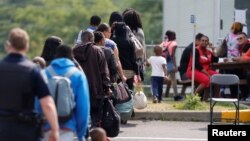 FILE - A group of asylum seekers wait to be processed after being escorted from their tent encampment to the Canada Border Services in Lacolle, Quebec, Aug. 11, 2017. 