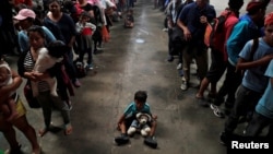 A child sits on the floor as Honduran migrants, part of a caravan trying to reach the U.S., queue to get a mat to rest at a migrant shelter in Guatemala City, Guatemala, Oct. 17, 2018.