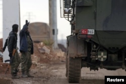 FILE - Turkish military vehicles drive by Free Syrian Army fighters, backed by Turkey, in the Syrian rebel-held town of al-Rai as they head toward the northern Syrian town of al-Bab, Jan. 9, 2017.