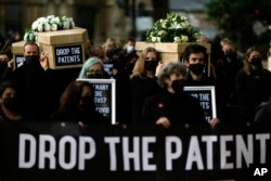 FILE - Global Justice campaigners carry fake coffins to highlight the number of COVID-19 deaths globally, in London, Oct. 12, 2021. Britain is taking part in a World Trade Organization intellectual property meeting to boost the number of vaccinations worldwide.