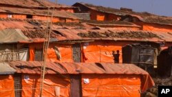 In this Jan. 28, 2018, photo, a Rohingya girl holds her brother while standing in front of their makeshift shelter at Jamtoli refugee camp in Cox's Bazar, Bangladesh. Their houses are often made of plastic sheets. 