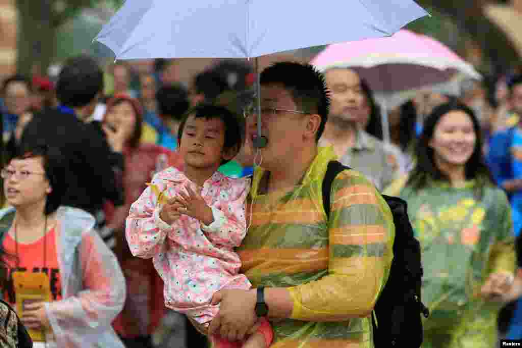 중국 상하이에서 상하이 디즈니 리조트 개장행사가 진행된 가운데, 한 관람객이 아이를 품에 안은채 우산을 입에 물고 입장하고 있다.