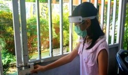 Seorang anak memakai masker dan dan pelindung wajah saat hendak keluar rumah untuk mencegah penularan virus corona di Surabaya, Jawa Timur, Selasa, 21 Juli 2020. (Foto: Petrus Riski/VOA).