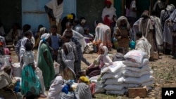 FILE - An Ethiopian woman sits on sacks of wheat to be distributed by the Relief Society of Tigray in the town of Agula, in the Tigray region of northern Ethiopia, May 8, 2021. 