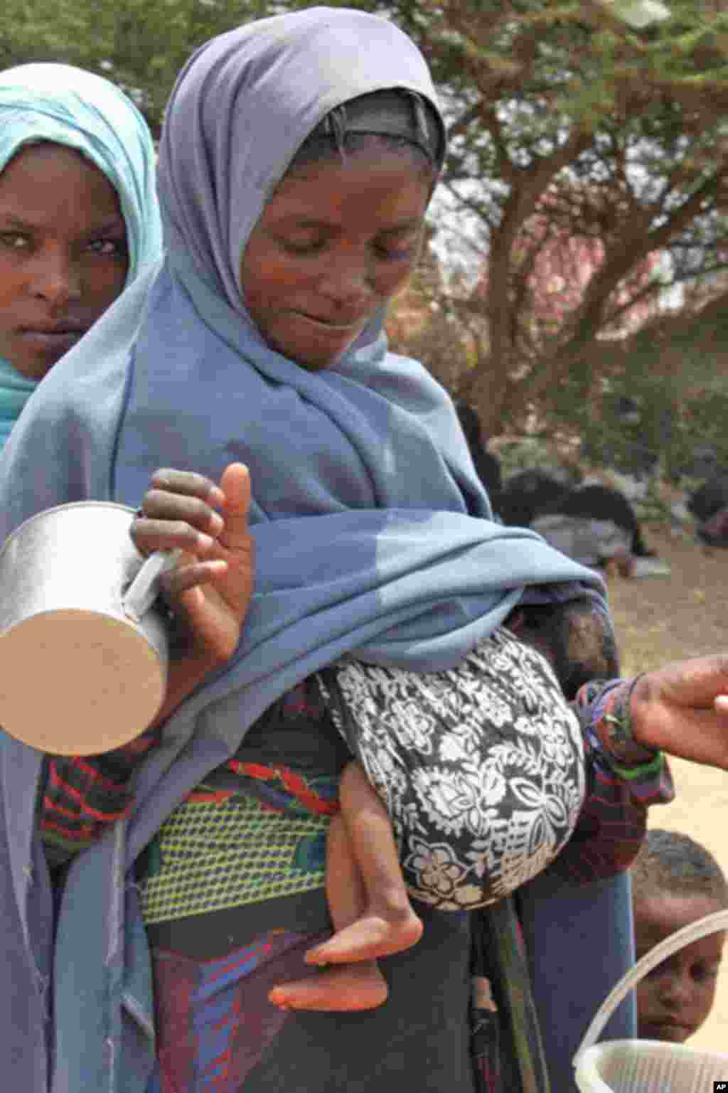 A woman arrives at a feeding center carrying her malnourished child. (VOA - P. Heinlein)