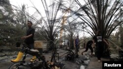 Beberapa orang berjalan melewati sisa-sisa kebakaran sumur minyak ilegal di Ranto Peureulak, Aceh, 25 April 2018. (Foto: Antara via Reuters)