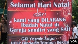 Spanduk raksasa di depan Istana Kepresidenan, Jakarta, umat Kristiani Indonesia, anggota Gereja GKI Yasmin (Bogor) dan Gereja HKBP Filadelphia (Bekasi) menggelar doa Natal (25/12). (Foto: VOA/Fathiyah)