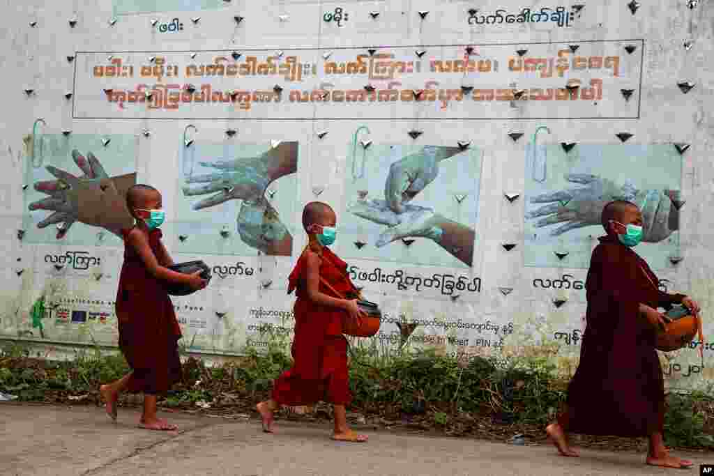 Buddhist novice monks wearing face masks walk past a COVID-19 awareness sign as they collect morning alms, in Yangon, Myanmar. 