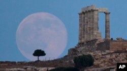 The full moon rises behind a tree next to the ruins of the ancient marble Temple of Poseidon, built in 444 BC, at Cape Sounion, southeast of Athens, on June 20, 2016. (AP Photo/Petros Giannakouris)