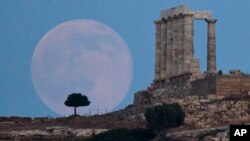 FILE - The full moon rises behind a tree next to the ruins of the ancient marble Temple of Poseidon, built in 444 BC, at Cape Sounion, southeast of Athens, on the eve of the summer solstice, June 20, 2016.