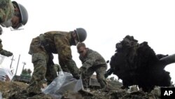 A U.S. Marine (R) and members of the Japan Self Defense Force clear tsunami debris at an elementary school in Ishinomaki, northern Japan, April 3, 2011.