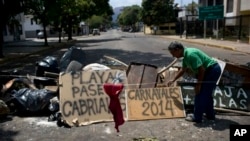 Man arranges board with spraypainted message that reads "Carnivals 2014," at a barricade set up by anti-government protesters, Valencia, Venezuela, Feb. 27, 2014.
