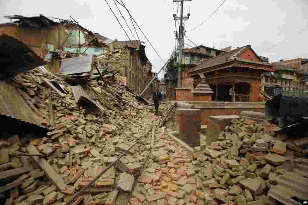 Seorang pria Nepal berjalan melewati reruntuhan yang disebabkan oleh gempa bumi hari Sabtu (25/4) di Bhaktapur, Nepal.