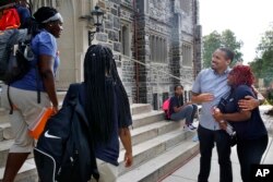 Anthony Guyton, dean of students at Washington Leadership Academy, hugs Indiae Gill, right, as she and other students arrive in the morning at the school in Washington, Aug. 23, 2017.