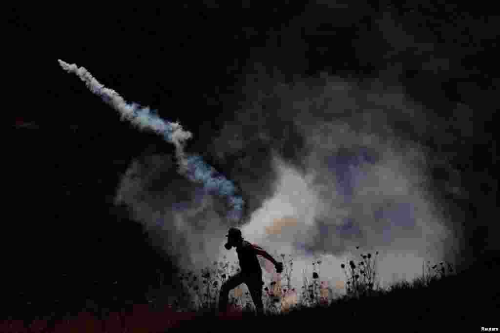 A Palestinian demonstrator returns a tear gas canister fired by Israeli troops during a protest against Jewish settlements and normalizing ties with Israel, in Asira al-Qibliya in the Israeli-occupied West Bank.