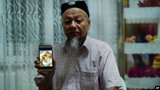 Ablikim Abliz holds up his phone with a photo of his uncle's family with an unknown Han Chinese man in Istanbul, Turkey, Aug. 22, 2018. He later heard that his uncle's front door was boarded up and sealed with police tape, and has not been able to contact him since.