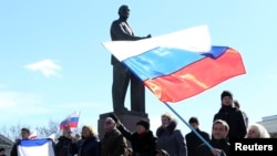 Para peserta dalam demonstrasi pro-Rusia melambai-lambaikan bendera Rusia di depan patung pendiri Soviet Vladimir Lenin di Simferopol (17/3). (Reuters/Sergei Karpukhin)