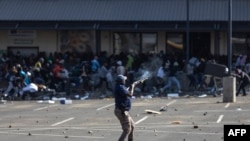 Un membre des services de police sud-africains (SAPS) tire des balles en caoutchouc sur des émeutiers pillant le centre commercial Jabulani à Soweto, au sud-ouest de Johannesburg, le 12 juillet 2021.