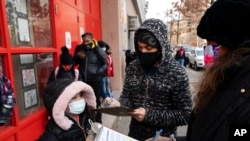 FILE - A parent with his child fills out a form granting permission for student COVID-19 testing at Szold Elementary School in New York, Dec. 7, 2021. U.S. officials are backing "test-to-stay" policies that will allow close contacts of infected students to remain in classrooms.