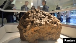 Reporters gather around a piece of a meteorite, which according to local authorities and scientists, was lifted from the bottom of the Chebarkul Lake, placed on display in a local museum in Chelyabinsk, Russia, Oct. 18, 2013.