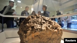 Reporters gather around a piece of a meteorite, which according to local authorities and scientists, was lifted from the bottom of the Chebarkul Lake in Chelyabinsk, Russia, Oct. 18, 2013.
