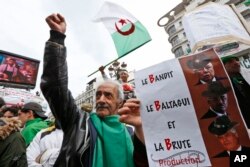 FILE - A demonstrator holds a sign referring to the three B's, Abdelkader Bensalah, Tayeb Belaiz et Noureddine Bedoui, interim rulers they want removed from their posts, during a rally in Algiers, Algeria, April 5, 2019.