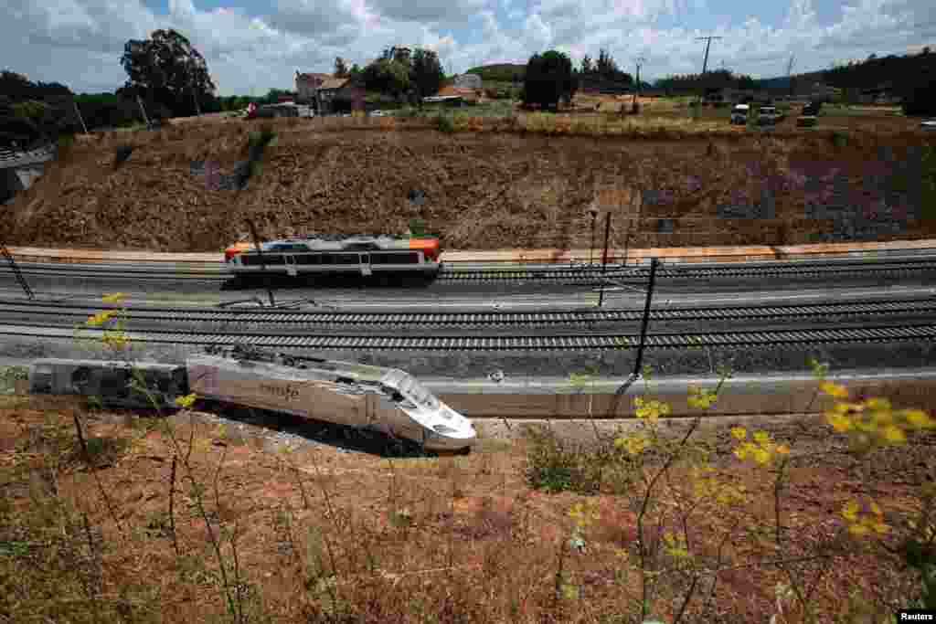 A passenger train passes by a wrecked train engine at the site of the train crash in Santiago de Compostela, northwestern Spain, July 26, 2013.&nbsp;