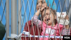 At a temporary refugee camp in Opatovac, Croatia, families complain they have been separated from relatives as children are passed back and forth over a fence, Sept. 22, 2015. (Heather Murdock/VOA)