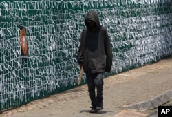 A pedestrian walks past the perimeter fence of the Presbyterian Church in Bedfordview, Johannesburg, South Africa, Wednesday, January 20, 2021. The fence is covered in ribbons to represent a person who died in the COVID-19 pandemic.  (Photo AP / Denis…