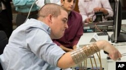 In this September 2014 photo provided by Ohio State University, Ian Burkhart participates in a study with neural bypass technology at The Ohio State University Wexner Medical Center in Columbus. A computer chip in Burkhart's brain reads his thoughts, decodes them, then sends signals to a sleeve on his arm, that allows him to move his hand. (Jo McCulty/Ohio State University Wexner Medical Center via AP)