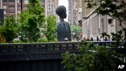 FILE - In this May 29, 2019 photo, visitors to the park gather near a bronze bust of a Black woman entitled "Brick House," by Chicago artist Simone Leigh in the High Line park in New York. (AP Photo/Bebeto Matthews)