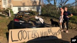 People stand near a sign warning looters in front of their house in Marianna, Florida, which was damaged by fallen trees during Hurricane Michael, Oct. 10, 2018. 