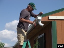 Jack Rose installs a gutter on the White Plume home. (VOA/J. Kent)