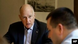 FILE - California Gov. Jerry Brown discusses a bill with budget analyst Chris Ferguson, right, in Sacramento, California, July 7, 2017. Brown and legislative leaders released a plan Monday to extend through 2030 California's cap-and-trade program, a key piece of the state's quest to fight climate change by drastically reducing emissions from greenhouse gases. 