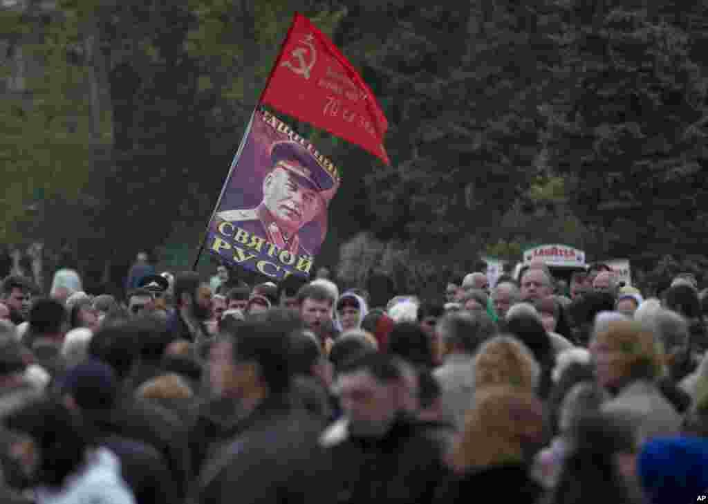 Replika bendera Soviet pada Perang Dunia II dan foto mantan penguasa Soviet, Joseph Stalin, dibawa warga yang berkumpul untuk upacara agama untuk mengenang para korban kebakaran sebuah gedung perdagangan di Odessa, Ukraina (10/5). (AP/Vadim Ghirda)
