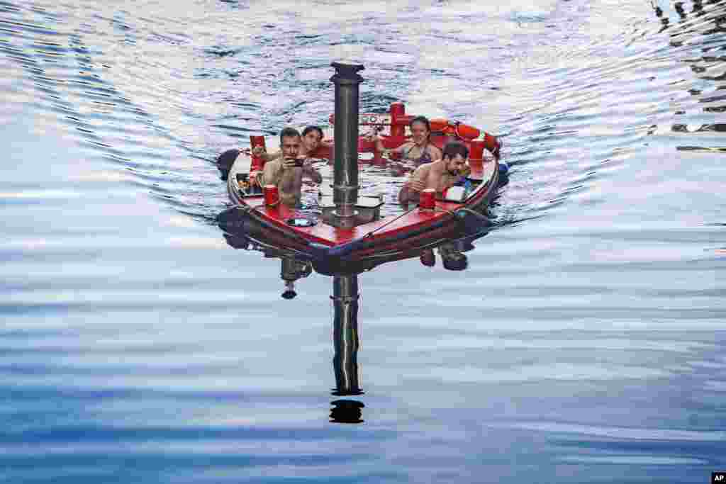 A group of people sit inside a hot tub boat sailing on the River Thames at Canary Wharf in London.