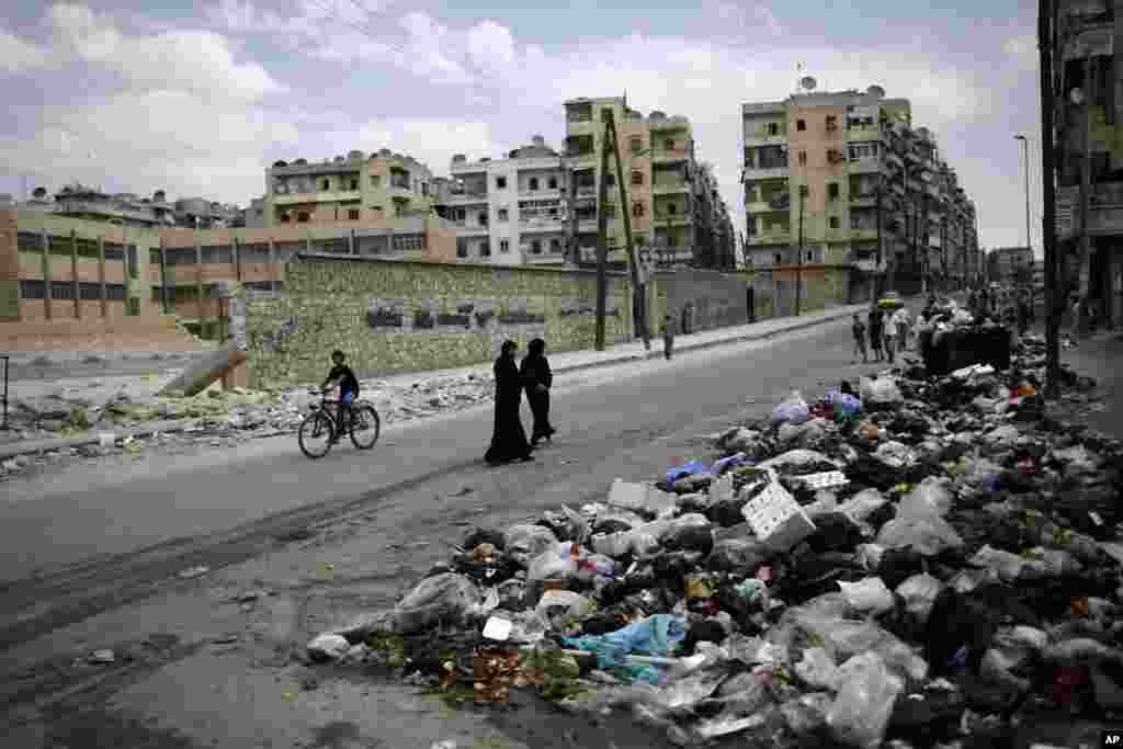 A Syrian woman looks back while walking with another woman past a pile of garbage left on a roadside in Aleppo, Syria, September 11, 2012. 