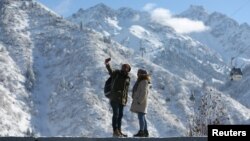 Sepasang turis berswafoto dengan latar belakang Gunung Tien Shan setelah turun salju di Almaty, Kazakhstan, 13 November 2018. (Foto: Reuters) 