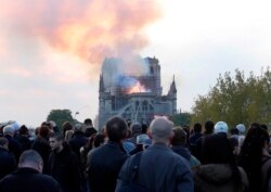 People watch as flames and smoke rise from Notre Dame cathedral as it burns in Paris, Monday, April 15, 2019.