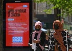 FILE - Pedestrians walk past a sign warning members of the public about a "Coronavirus variant of concern," in Hounslow, west London, Britain, June 1, 2021.