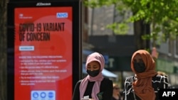 FILE - Pedestrians walk past a sign warning members of the public about a "Coronavirus variant of concern," in Hounslow, west London, Britain, June 1, 2021.
