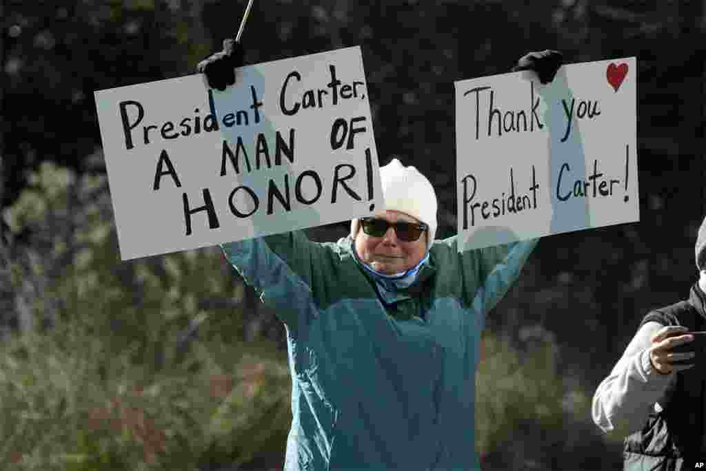 A person holds signs as the hearse containing the casket of former President Jimmy Carter, pauses at the Jimmy Carter Boyhood Farm in Archery, Georgia, Jan. 4, 2025. Carter died Dec. 29 at the age of 100.