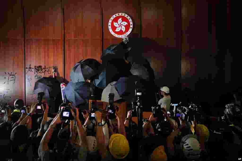 Journalists film a protester defaces the Hong Kong emblem inside the meeting hall of the Legislative Council in Hong Kong.