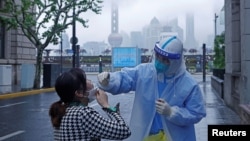 中國上海，一名穿戴防護裝備的醫務人員正為一名居民採集拭子樣本，進行核酸測試（2022年4月26日）。