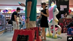 FILE - A man carries bags containing toys from the FAO Schwarz as people shop at the newly open FAO Schwarz toy store in Beijing, June 1, 2019. 