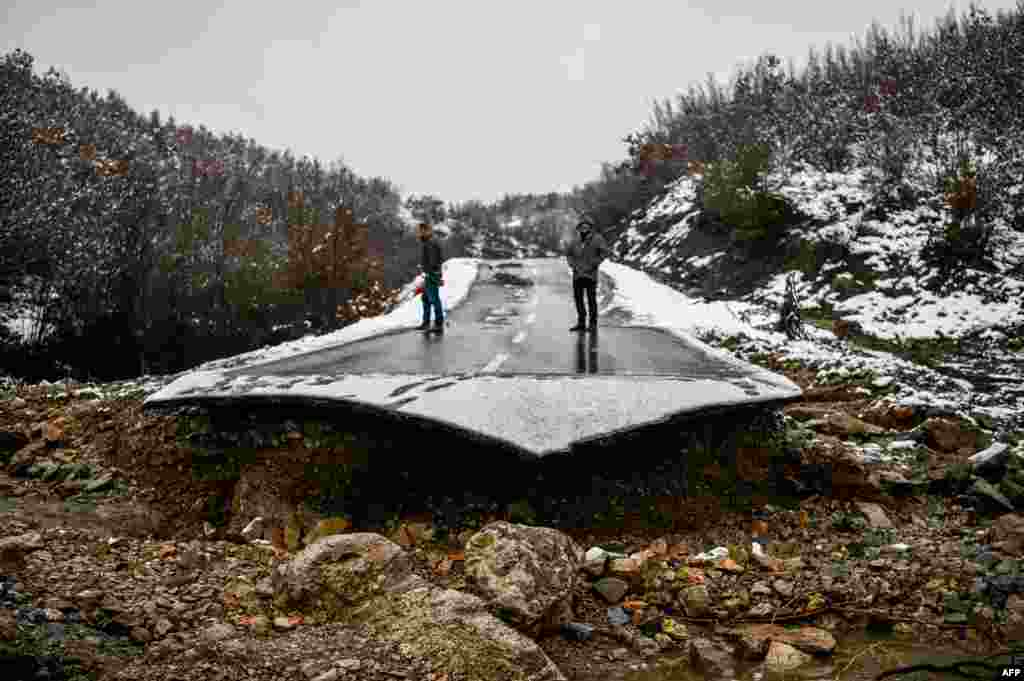 Two men stand on a collapsed road due to heavy floods in the village of Sferke, Kosovo.