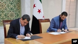 In this photo released by Syrian state news agency SANA, Syria's interim President Ahmad al-Sharaa, right, and Mazloum Abdi, the commander of the U.S.-backed Kurdish-led Syrian Democratic Forces, sign a deal in Damascus, Syria, March 10, 2025. (SANA via AP)