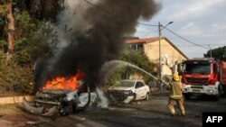 Vatrogasci gase automobil koji je pogođen u gradu Aškelonu na jugu Izraela (Foto: Menahem KAHANA/AFP)