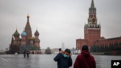 FILE - A man puts on a protective face mask as he stands with another person in a deserted Red Square in Moscow, Russia, Oct. 28, 2021.